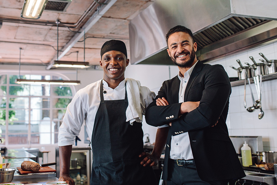 Specialized Business Insurance - Restaurant Owner Standing With His Chef in the Kitchen Smilling